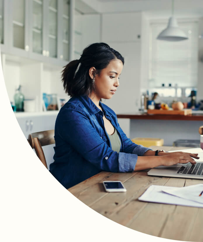 woman types on her laptop at a kitchen table 