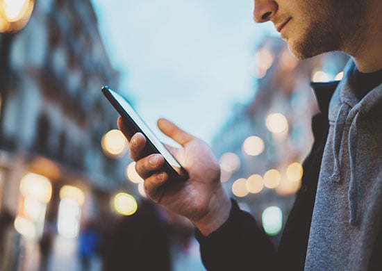 Man checking his phone while walking in a city.
