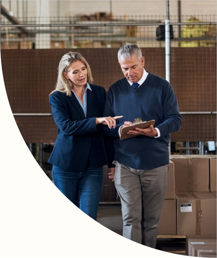 Two business employees reviewing data on a paper report in a warehouse