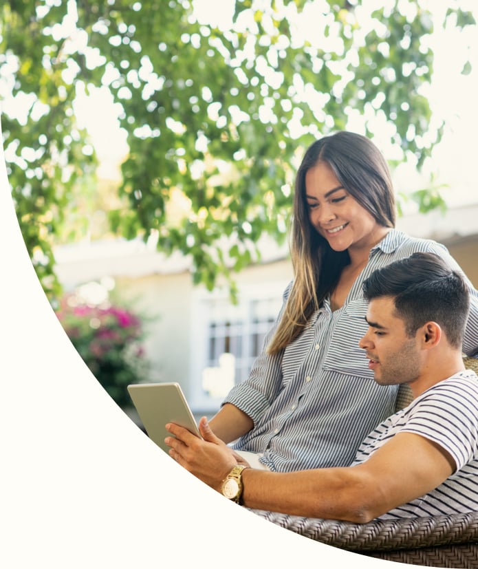A young couple relax in their backyard on a comfy chair while they collectively shop on their tablet