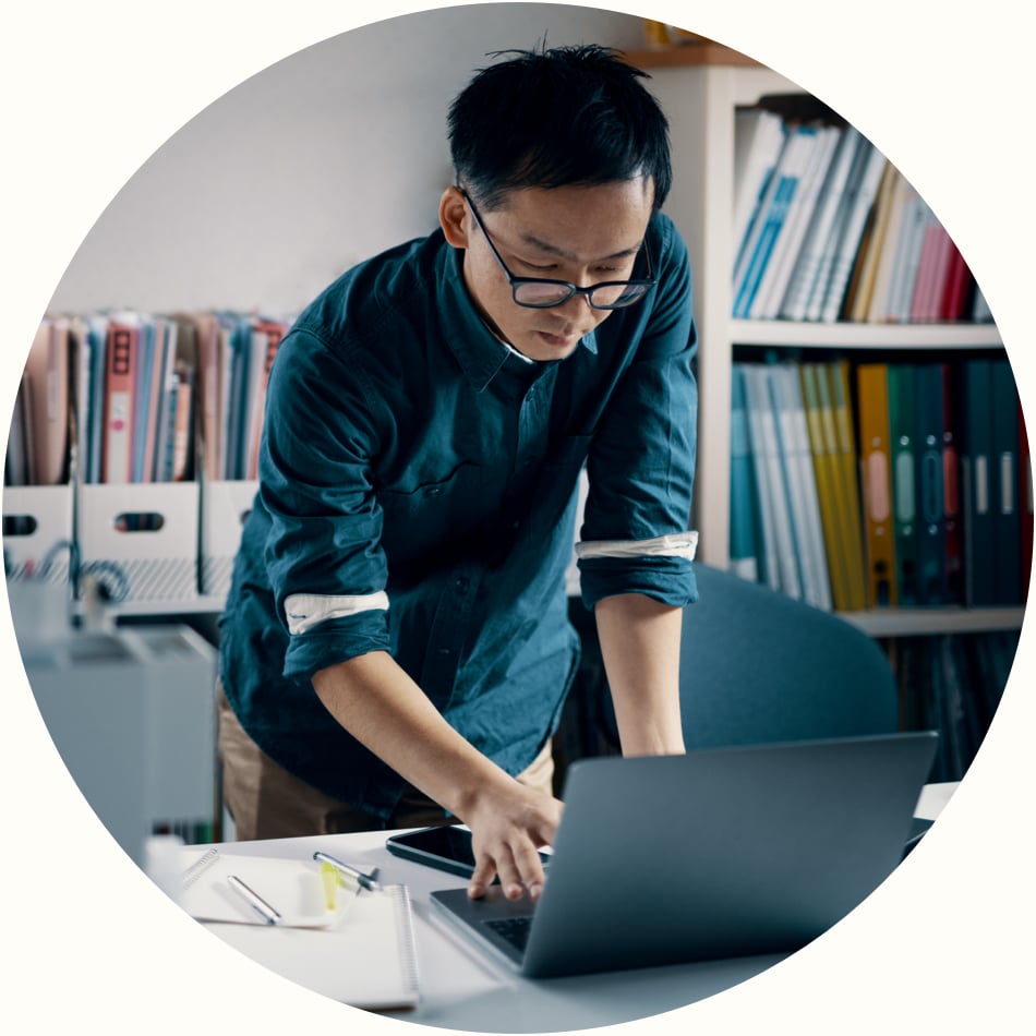 focused professional man wearing glasses stands at desk and reviews reports on a laptop computer