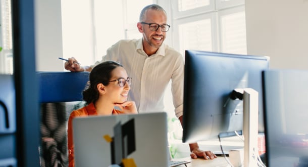 male and female coworkers smiling while collaborating in office on computers together