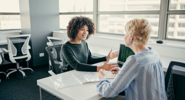 Two women in office discussing loan details over desk and computer