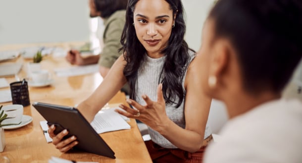 woman speaking with female colleague over tablet