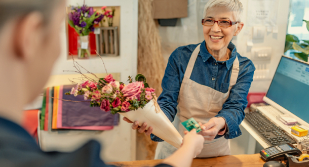 Mature, gray hair, flower shop owner receiving a payment from a customer with a credit card
