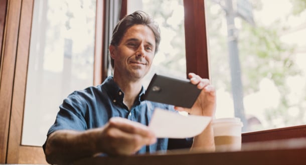 A mature smiling man takes a picture with his smart phone of a check for digital electronic depositing, also known as Remote Deposit Capture