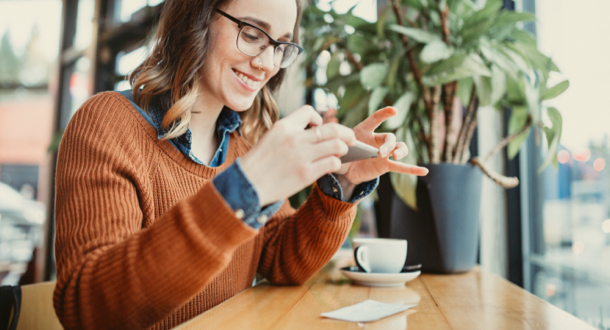 A smiling young woman takes a picture with her smart phone of a paycheck for digital electronic depositing, also known as 