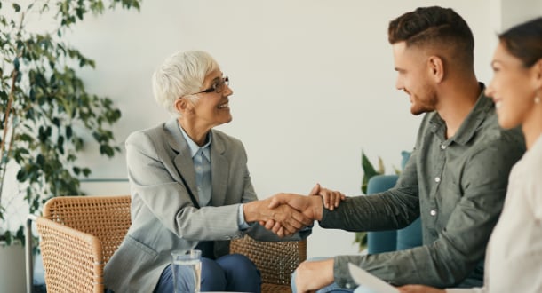 Happy mature financial advisor shaking hands with her clients after successful meeting in the office.