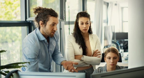 coworkers standing over computer detecting fraud