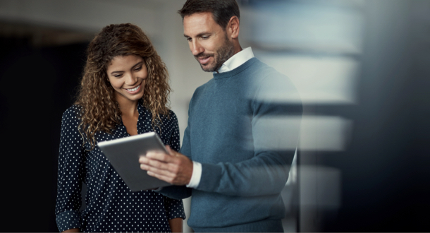 two colleagues working on a digital tablet together while standing in a large office