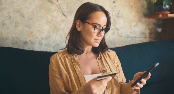 young woman using a smartphone and credit card on the sofa