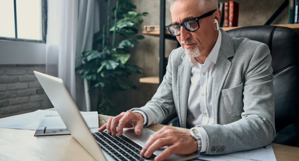 adult man in glasses working in the office while typing on laptop while using wireless headphones
