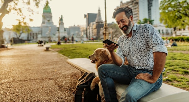 Mature Latino man with beard any stylish casual clothing in springtime day on cell phone in park