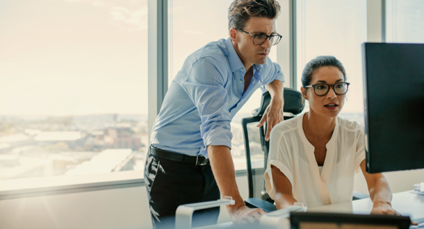 Two corporate professionals working on computer together in office.