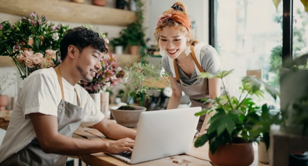 Smiling young Asian couple, the owners of small business flower shop, discussing over laptop on counter