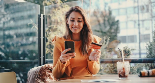 Young girl in orange sweater is sitting at the café, shopping online