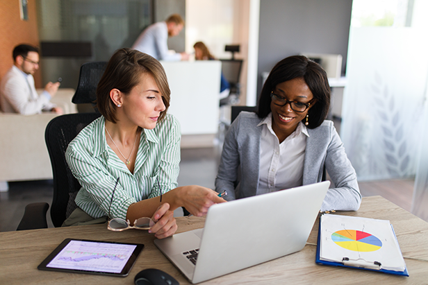 Two businesswomen collaborating in the office using laptop, digital tablet, and charts.