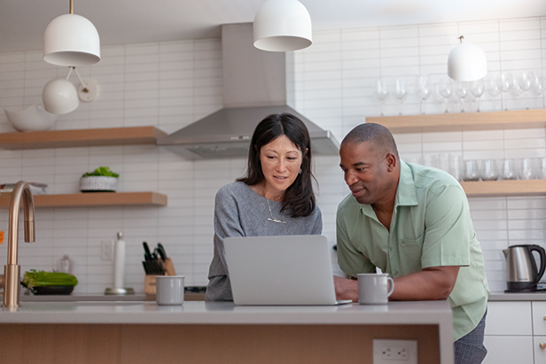 Happy couple at home in kitchen using laptop computer to easily move money between their accounts.