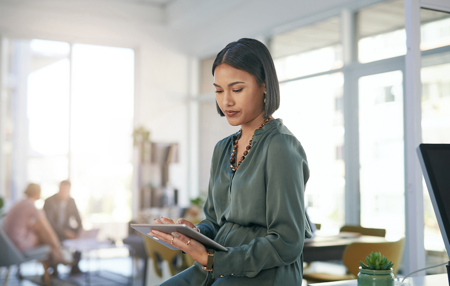 stylishly dressed woman reviews data on tablet in a bright, open concept modern office